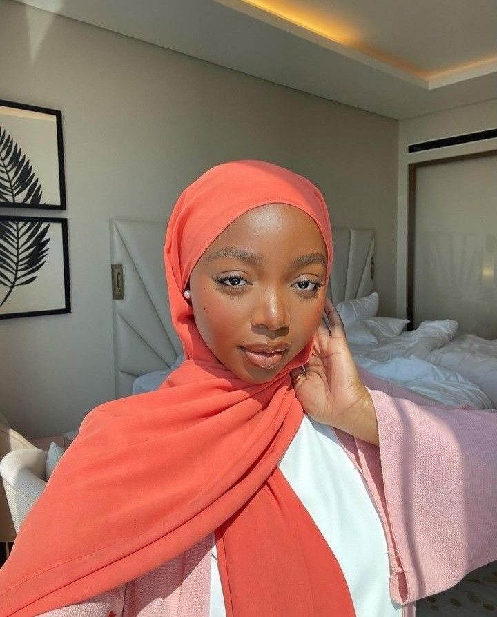 Close-up selfie of Rodia in a coral hijab, hand resting at her cheek.