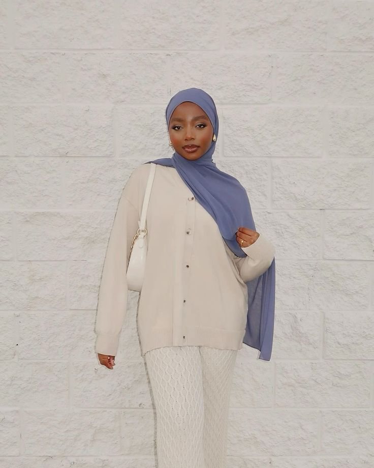 Rodia standing against a white stone wall in a cream cardigan and lilac hijab.